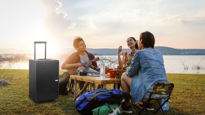 Sekolompok anak muda sedang bernyanyi bersama dengan menggunakan trolley speaker dari Sharp di tepi danau